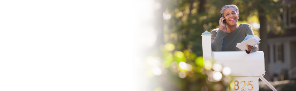 Women leaning on a mailbox with mail in hand and talking on a cell phone.
