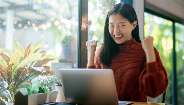 woman celebrating while looking at laptop